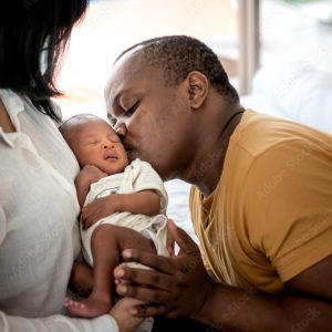 An African-American couple holding their baby and father kissing on cheek