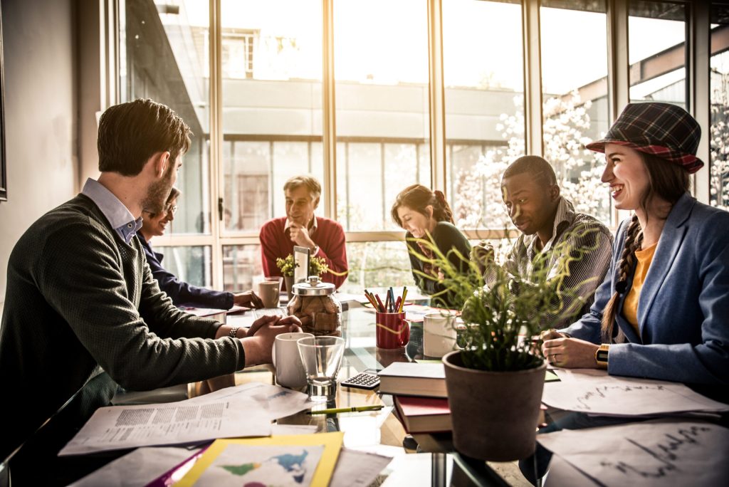 Six colleagues seated around a glass conference table, discussing documents in a sunlit meeting room.